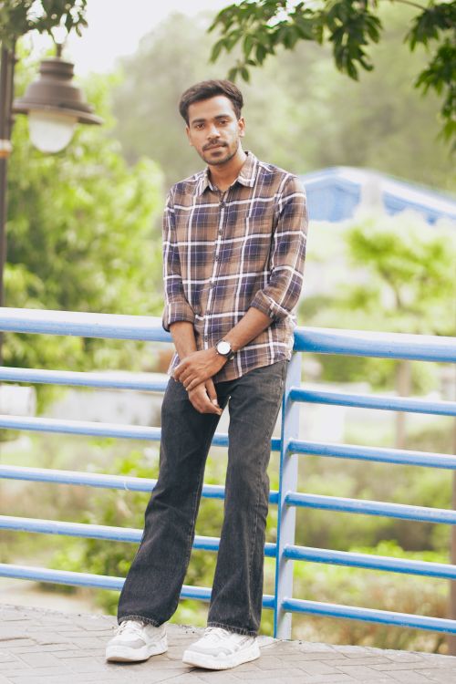 Free A stylish man in casual attire poses outdoors in a park setting. Stock Photo