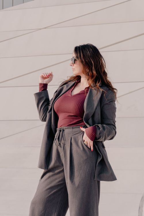 Free Woman in a stylish grey suit poses confidently against a modern architectural background. Stock Photo