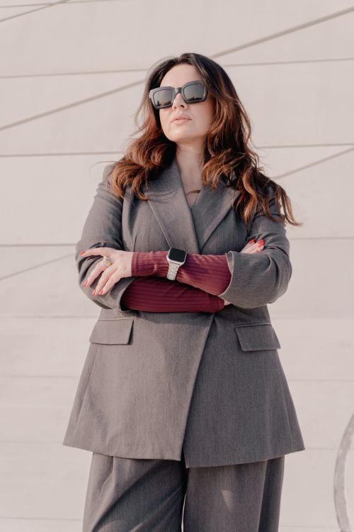 Free Confident woman in a gray suit and sunglasses standing with arms crossed outdoors on a sunny day. Stock Photo