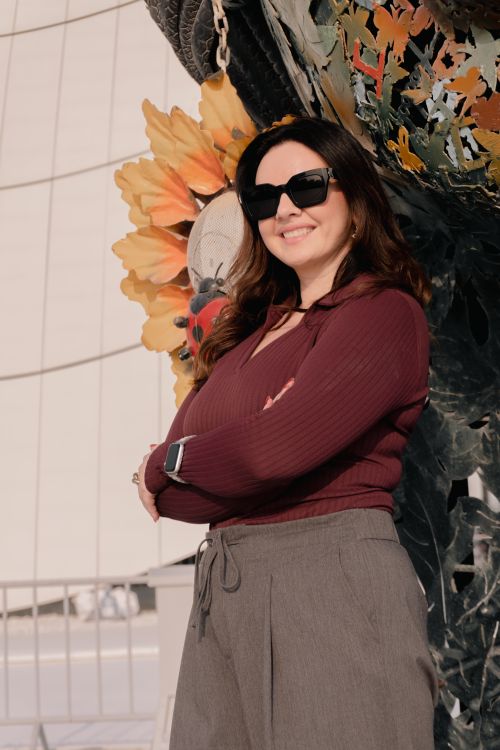 Free Smiling woman in sunglasses poses confidently in front of colorful sculpture outdoors. Stock Photo