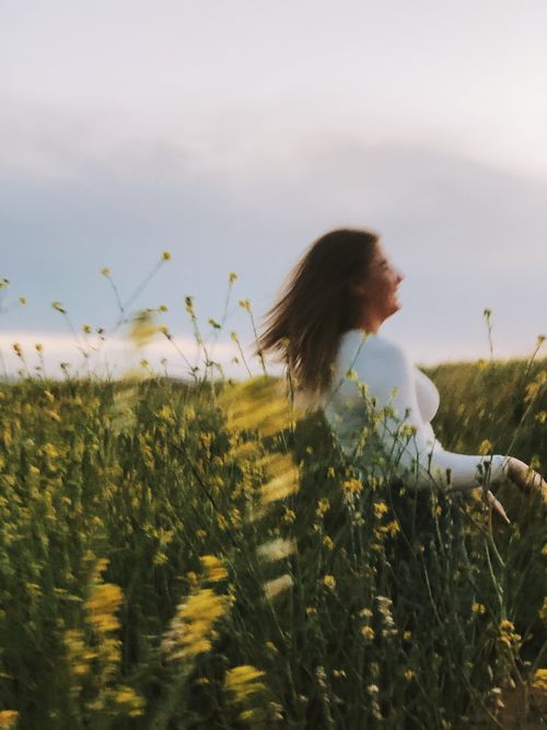 Free A woman joyfully spins in a wildflower field at sunset, capturing motion and nature's beauty. Stock Photo
