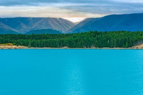 Free Tranquil lake with mountains and forest under a cloudy sky. Stock Photo