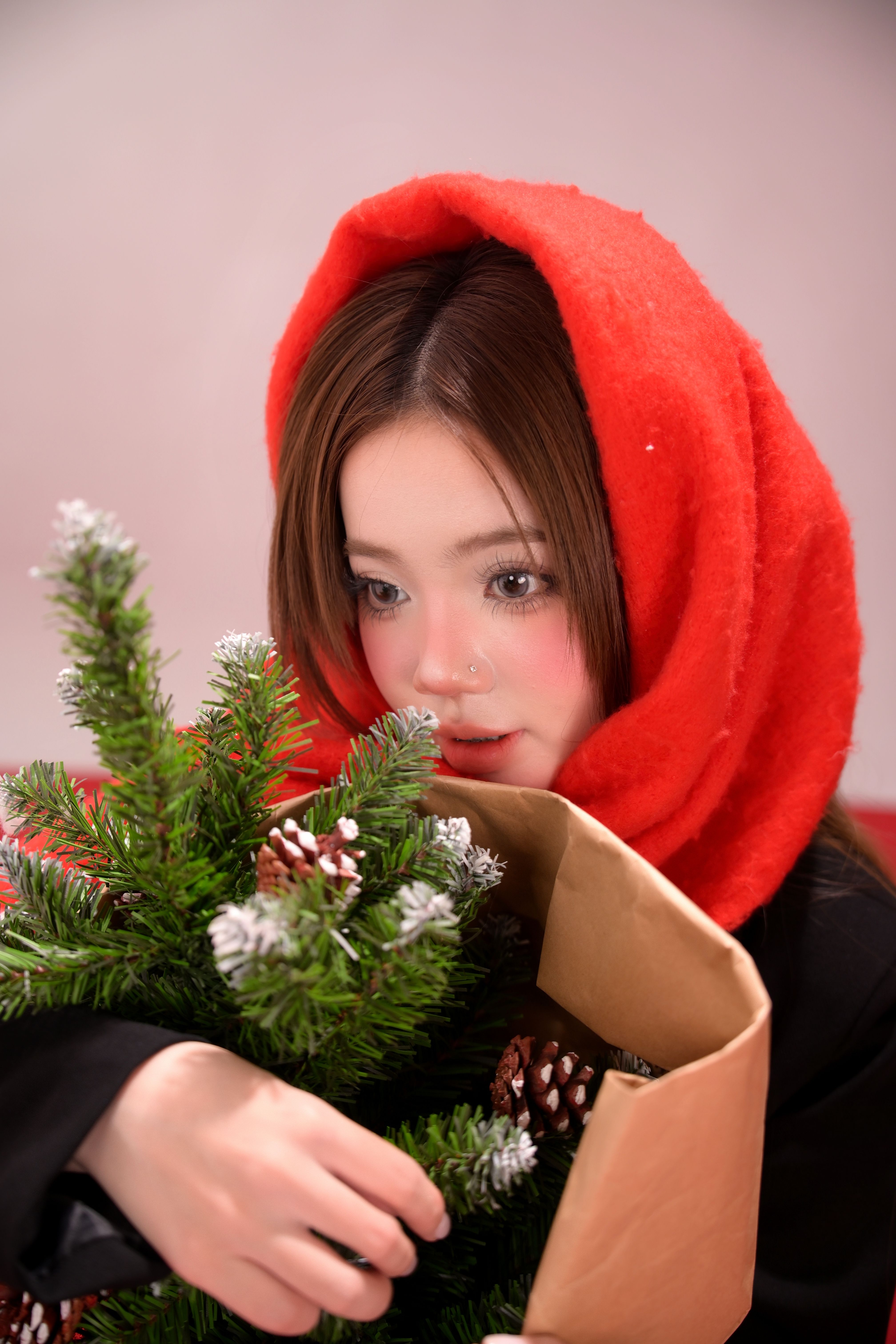 Young woman wearing red scarf holds a paper bag with a small Christmas tree.