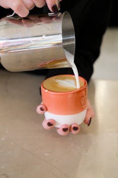 A skilled barista carefully pours beautiful latte art into a vibrant ceramic cup.