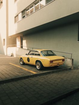 A classic yellow sports car parked in a sunlit urban environment, exuding vintage charm.