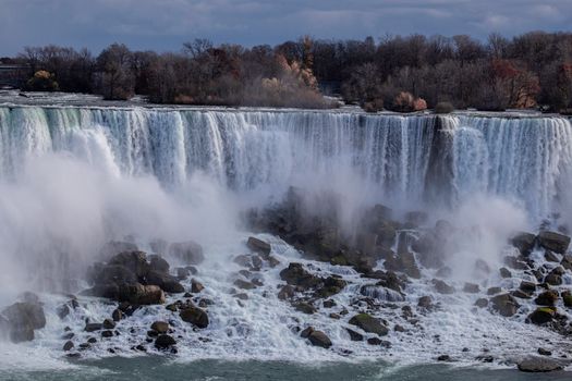 Scenic Niagara Falls with powerful water flow and autumn foliage under a cloudy sky.