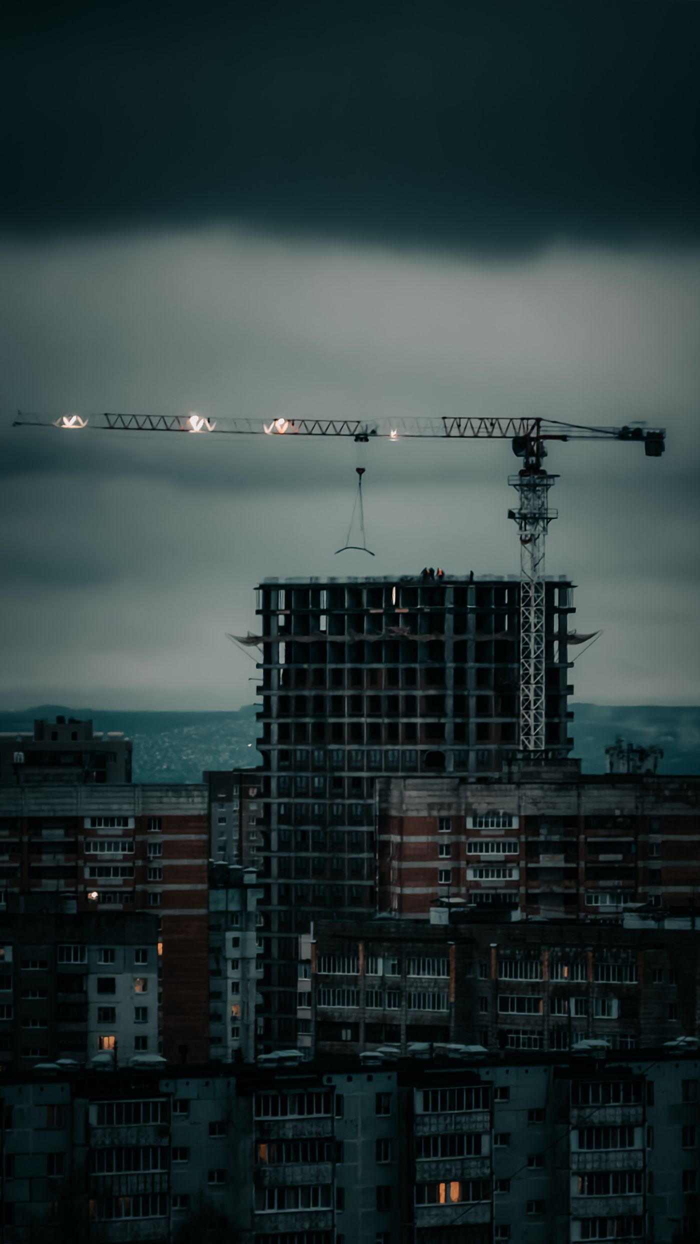 A construction site with a crane at dusk, a building rising against the city skyline