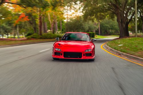 Free Vibrant red sports car drives through a scenic curved road lined with lush greenery. Stock Photo
