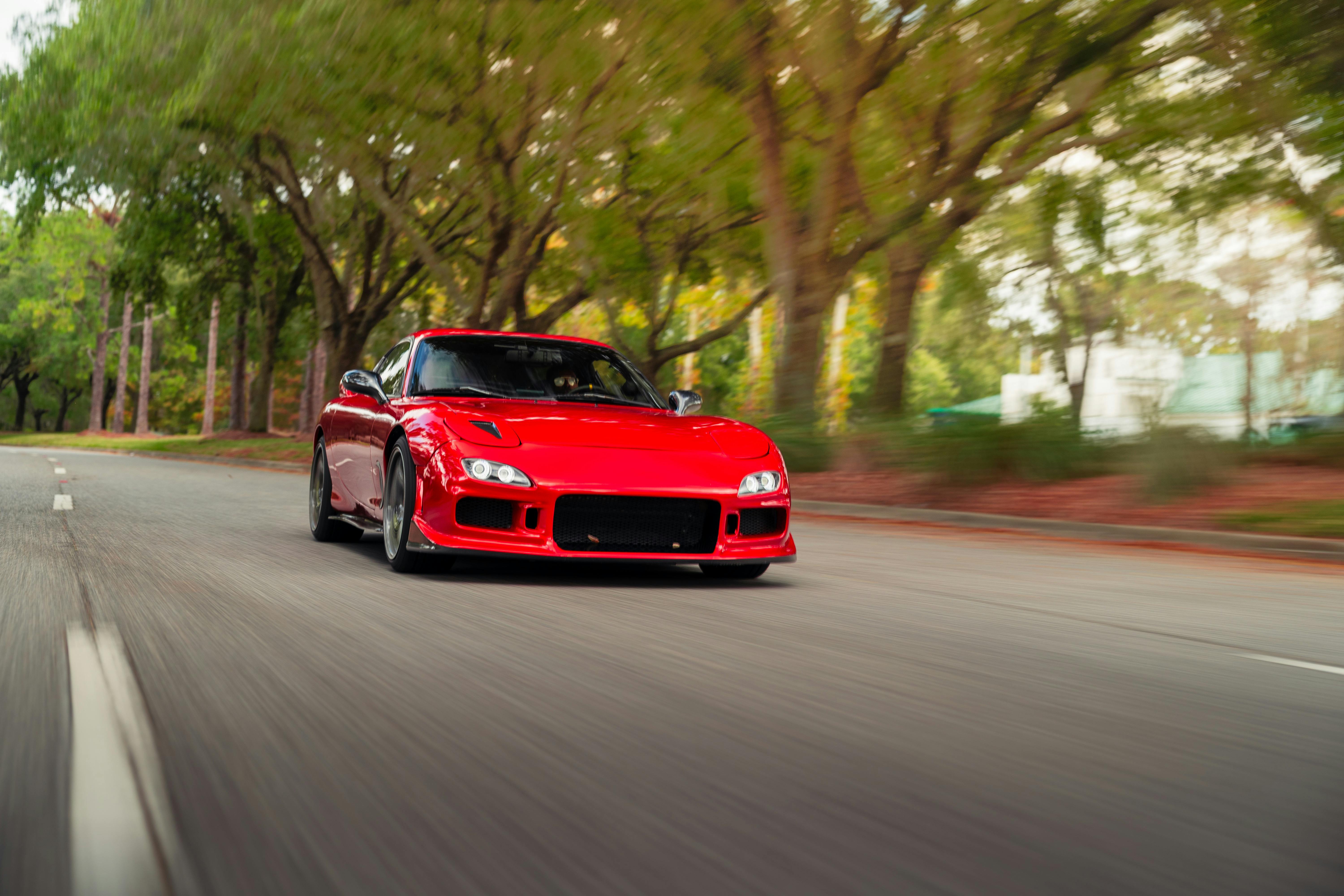 A sleek red sports car in motion on a picturesque, tree-lined road.