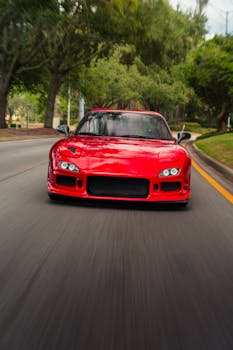 Red sports car speeding down a tree-lined road in motion blur.