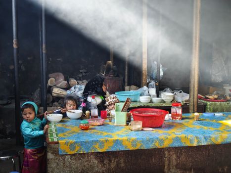 Three children savor a meal in a homely rustic kitchen under a beam of sunlight.