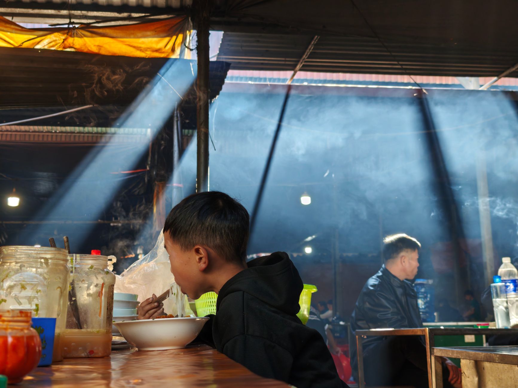 A young boy dining in a rustic indoor market with beams of light filtering through.