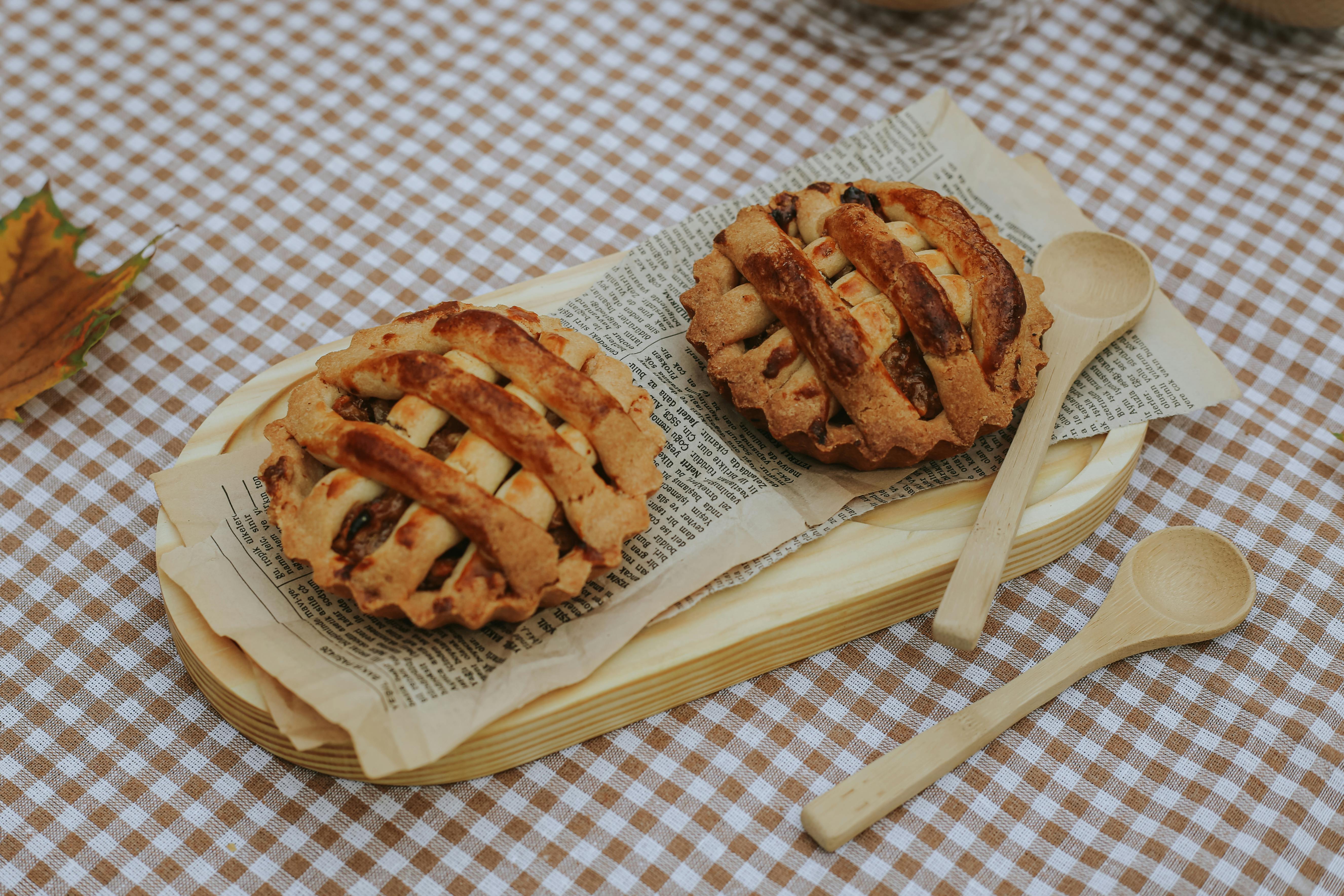 Rustic mini apple pies on a checkered tablecloth with wooden spoons and autumn leaves.
