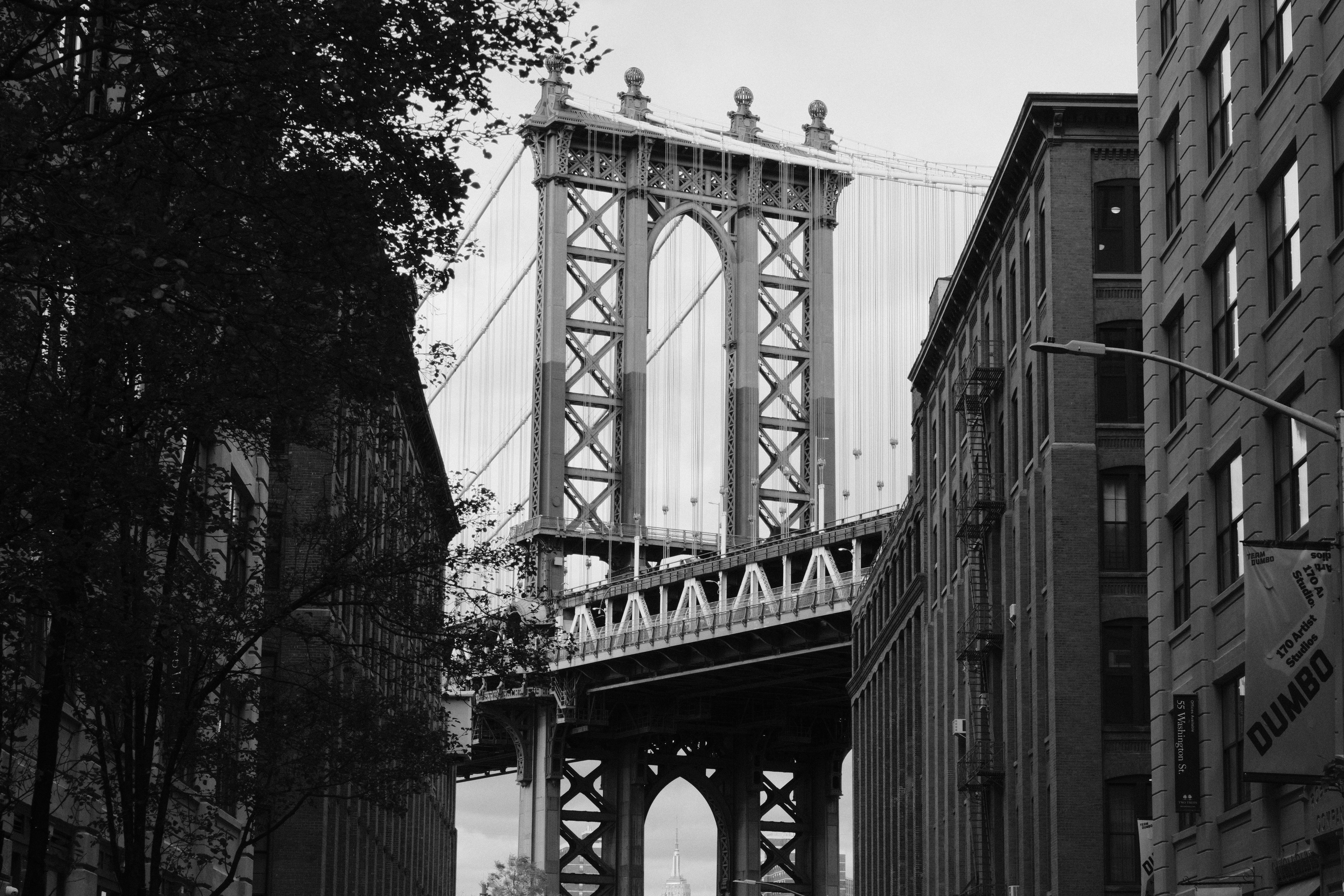 Black and white photograph capturing the iconic Manhattan Bridge framed by buildings in DUMBO, Brooklyn.