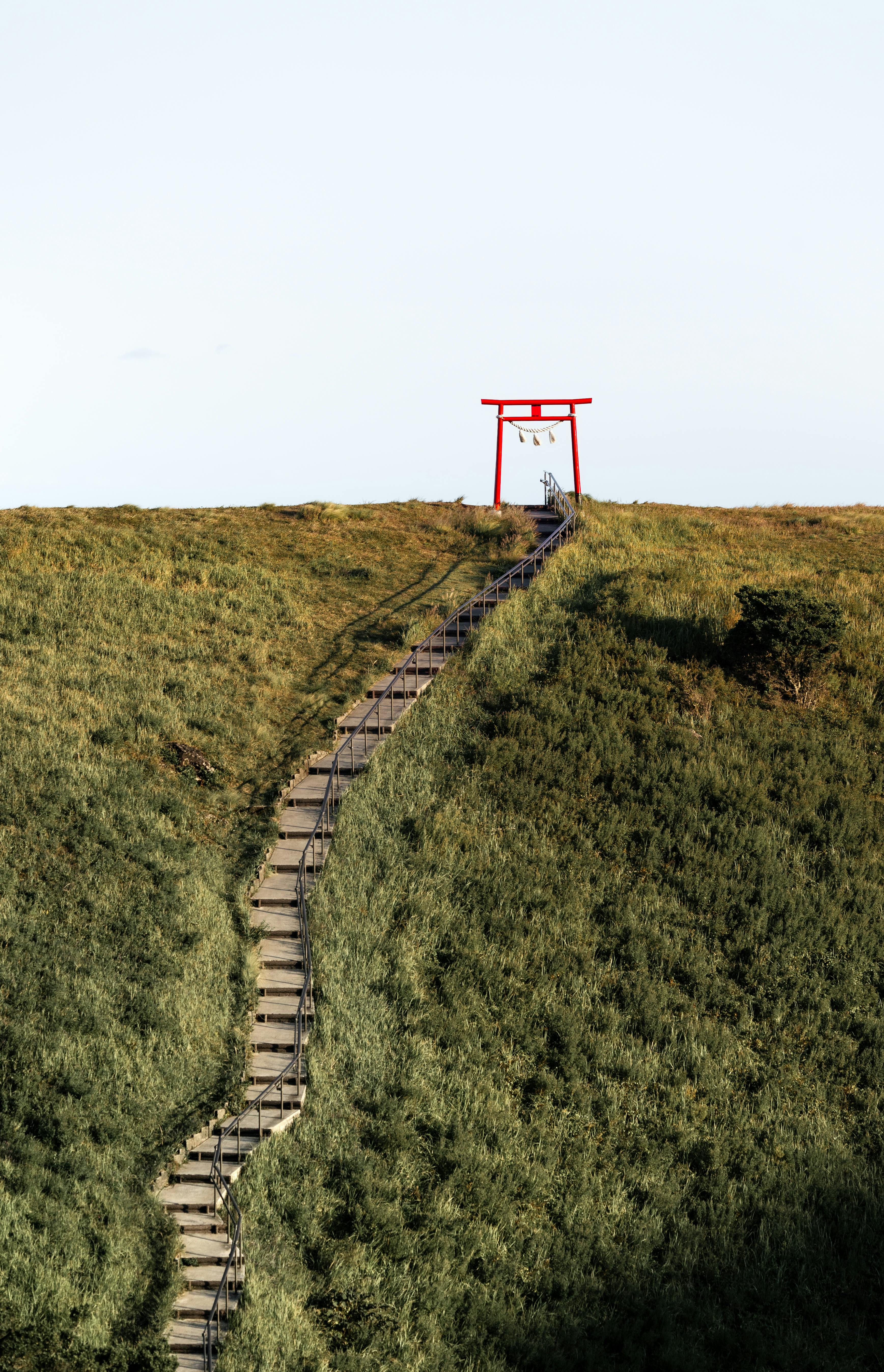 Scenic view of a hilltop Torii gate in Japan featuring lush green landscapes and stone steps.
