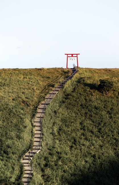 Scenic view of a hilltop Torii gate in Japan featuring lush green landscapes and stone steps.