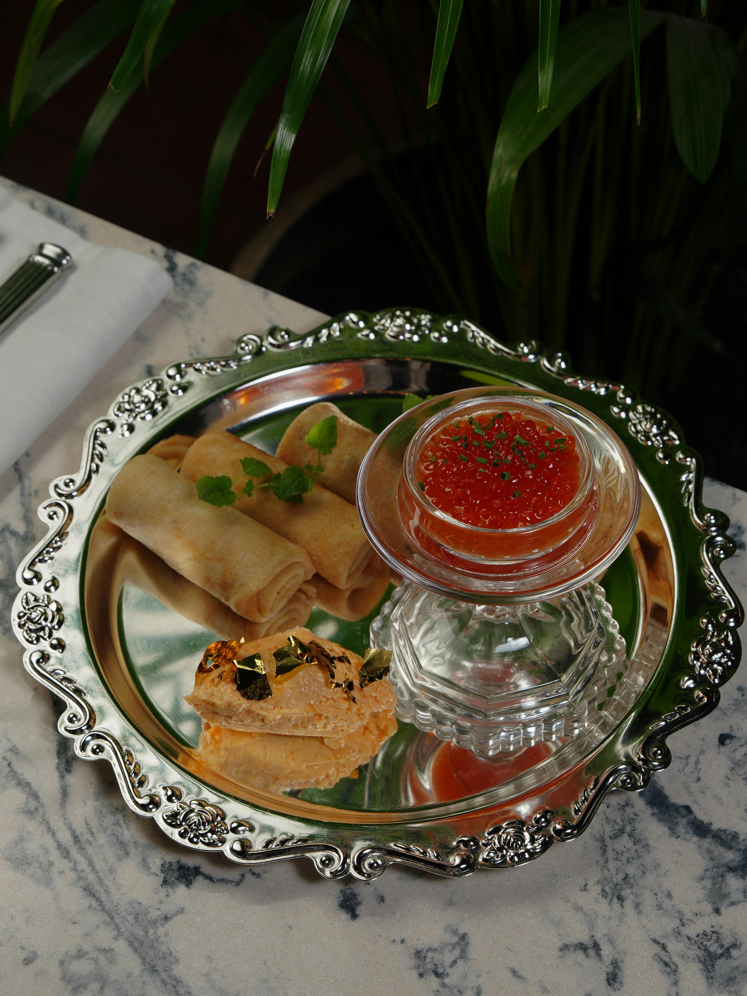 Elegant appetizer tray with red caviar, spring rolls, and gourmet bread on a ornate tray.