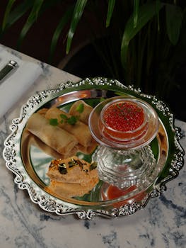 Elegant appetizer tray with red caviar, spring rolls, and gourmet bread on a ornate tray.