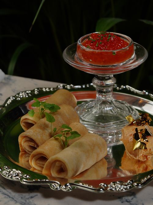 Free Elegant platter of rolled crepes, salmon roe, and gold leaf pastries on a marble table. Stock Photo