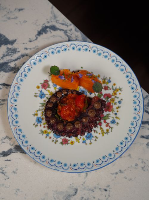 Free Exquisite plated octopus with vibrant garnish on decorative floral plate, perfect for gourmet food enthusiasts. Stock Photo