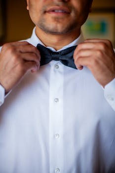 Close-up of a man adjusting his bow tie while dressed in a formal white shirt.