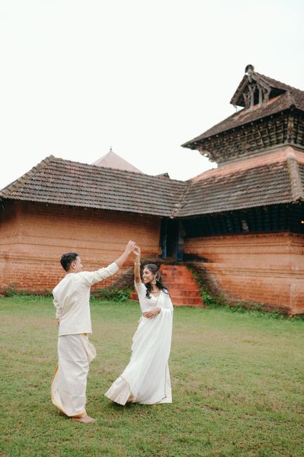 A couple in traditional Indian attire dancing outdoors by a historic building.