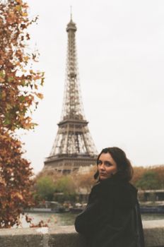 A woman enjoys the scenic view of the Eiffel Tower in Paris amidst autumn foliage.