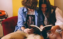 Young Couple Reading Together Indoors on Sofa