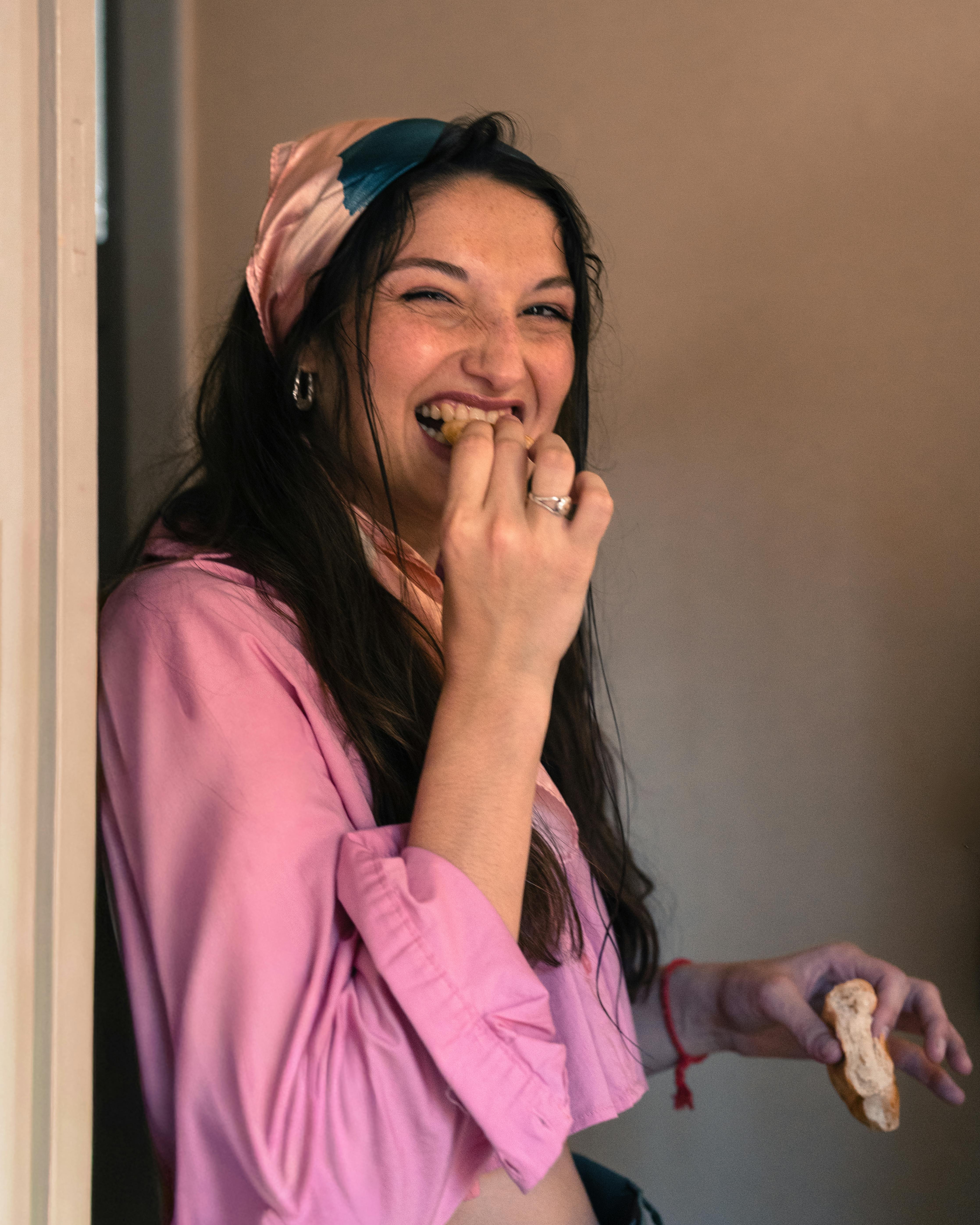 Kostnadsfria Leende kvinna i rosa kläder njuter av ett mellanmål inomhus. Avslappnad och glad atmosfär. Stock foto