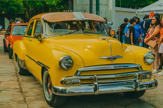 A vibrant yellow vintage car displayed at a street festival in Comitán de Domínguez, México.