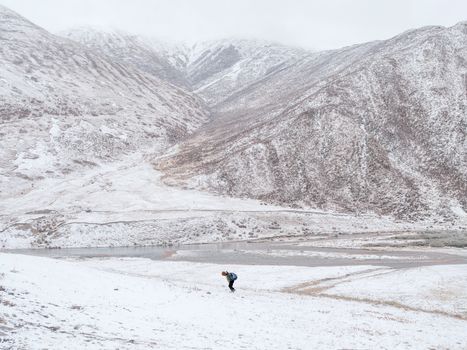 Solitary hiker traverses snowy mountainside in serene winter landscape.