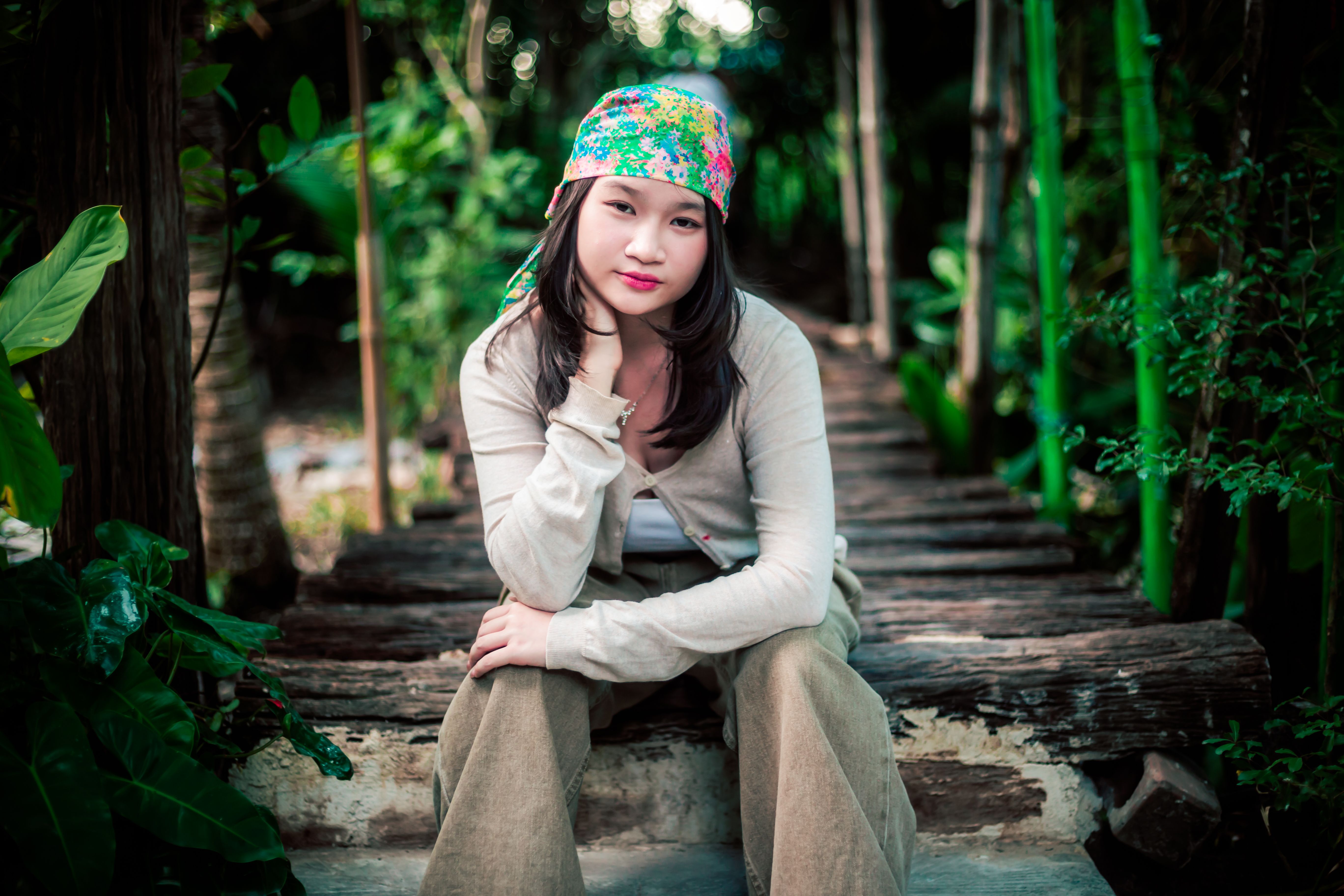 Portrait of a young woman wearing a headscarf on a rustic bridge surrounded by lush greenery.