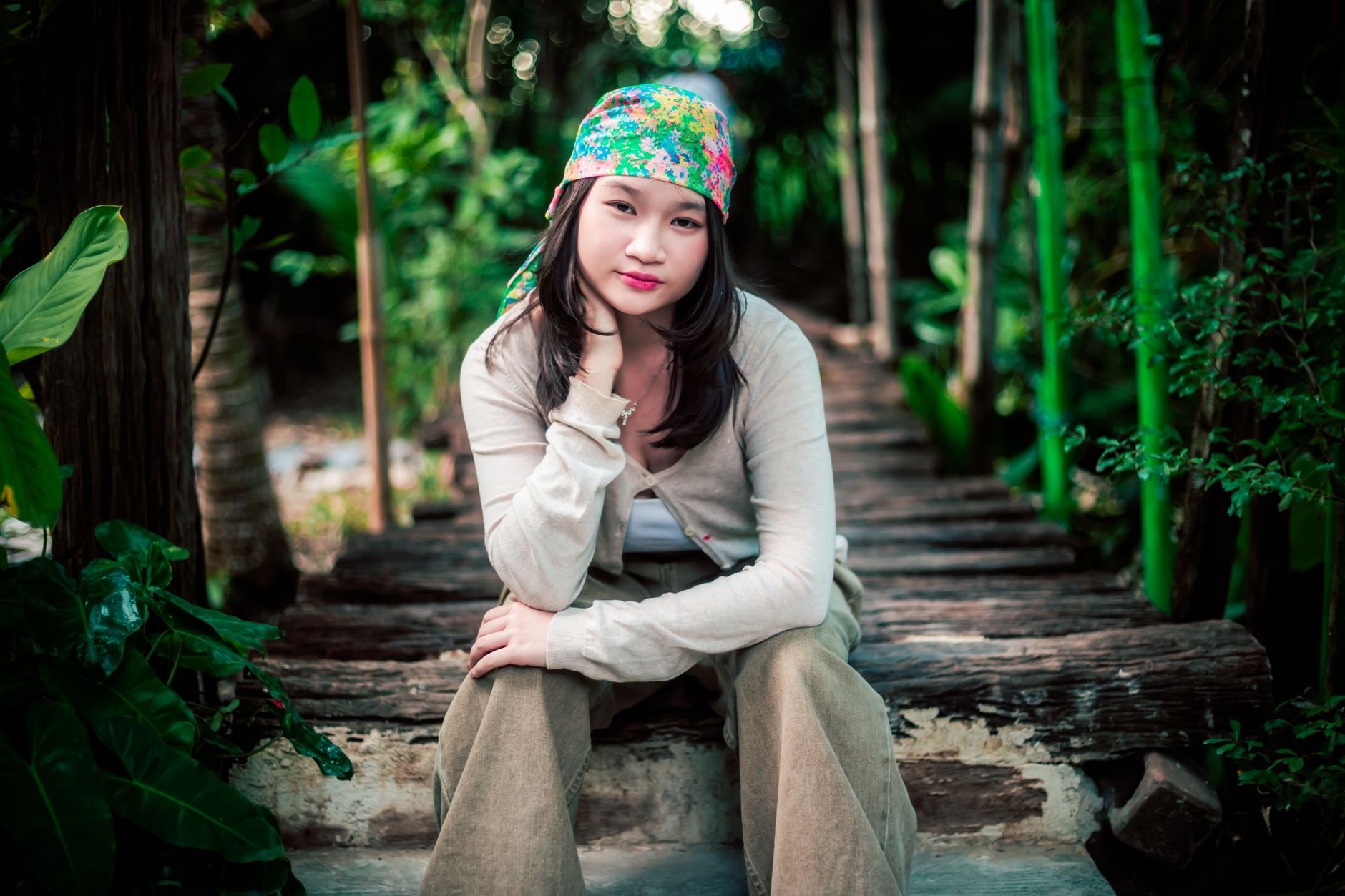 Portrait of a young woman wearing a headscarf on a rustic bridge surrounded by lush greenery.