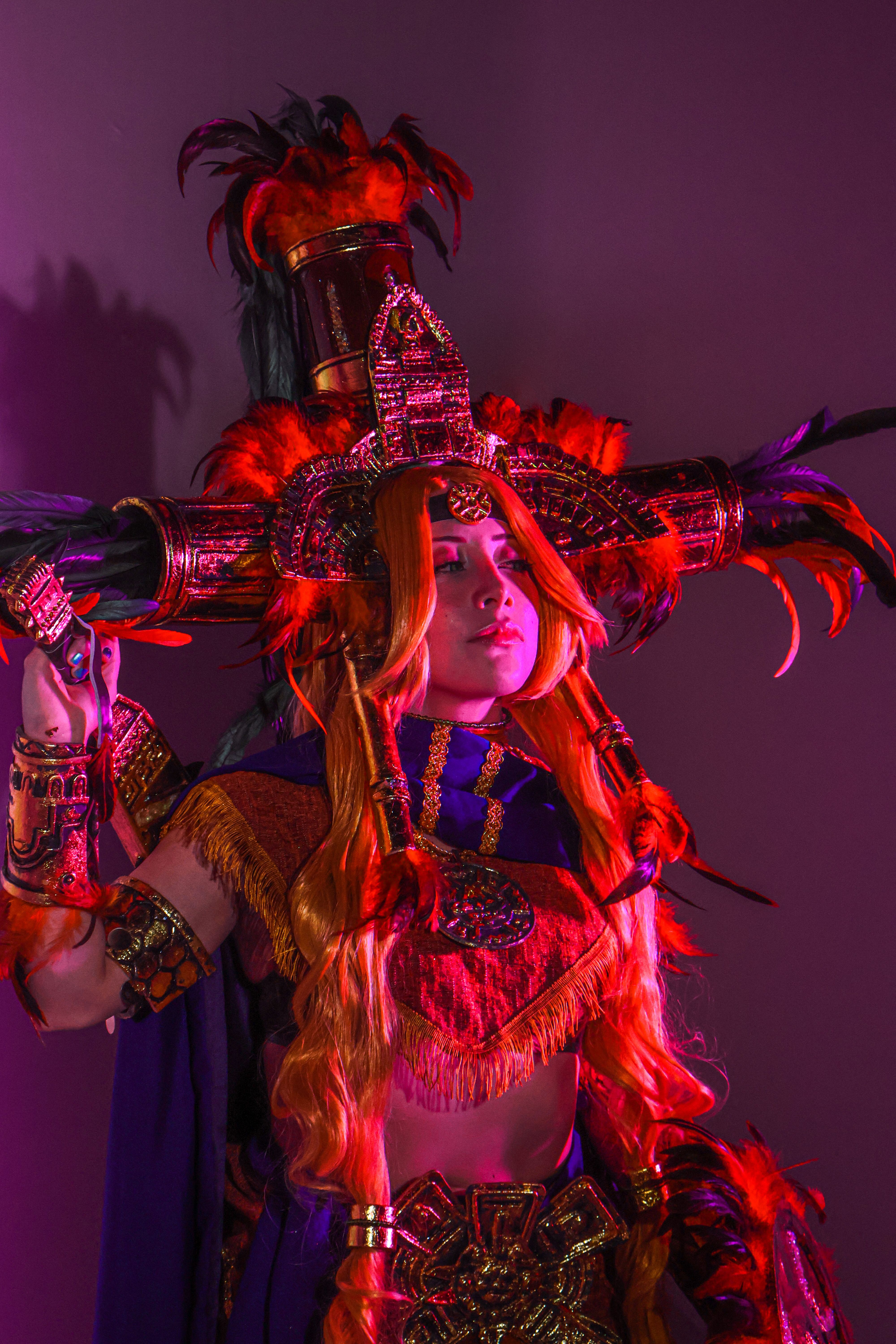 A person in a detailed, colorful costume with feathers and dramatic lighting, evoking a fantasy or cultural theme.