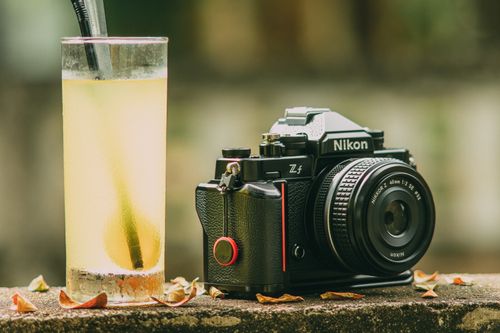 Free A vintage-style camera next to a glass of lemonade on a sunny day outdoors. Stock Photo
