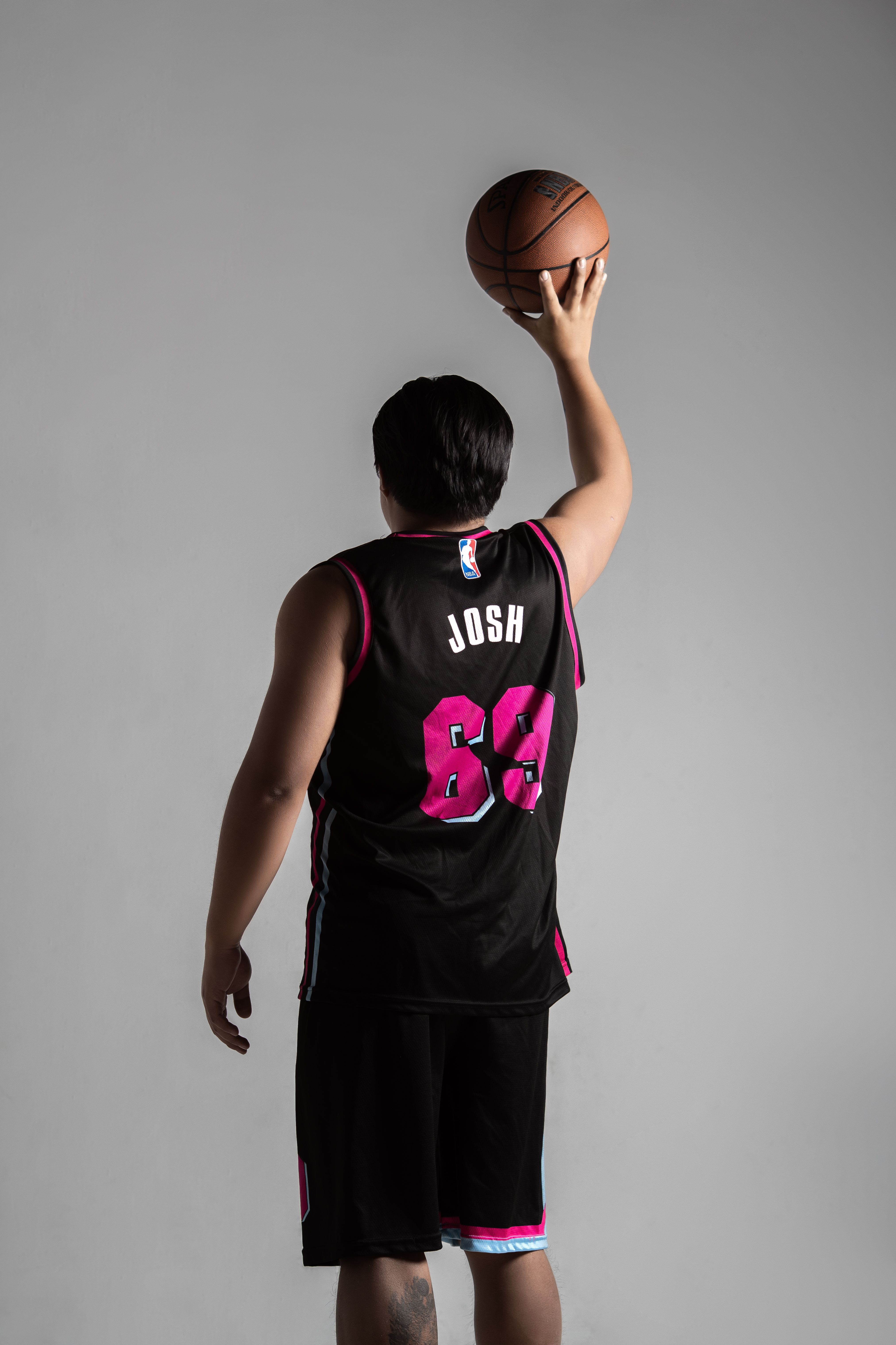 Basketball player in jersey holding ball ready to shoot against gray background.