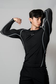 Young man in black sportswear flexing muscles against a neutral backdrop.