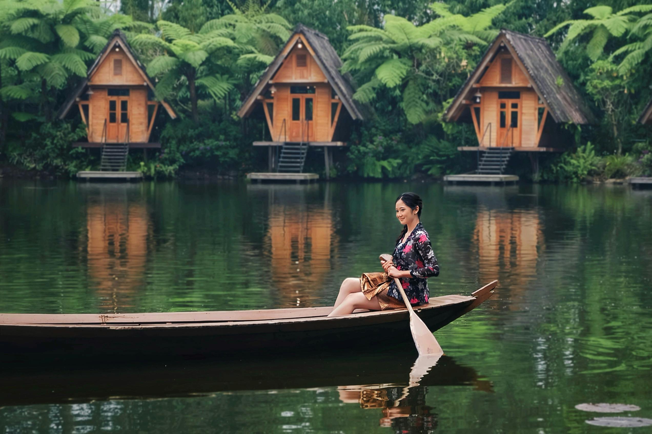 A woman enjoying a peaceful canoe ride on a lake surrounded by wooden huts and lush greenery.