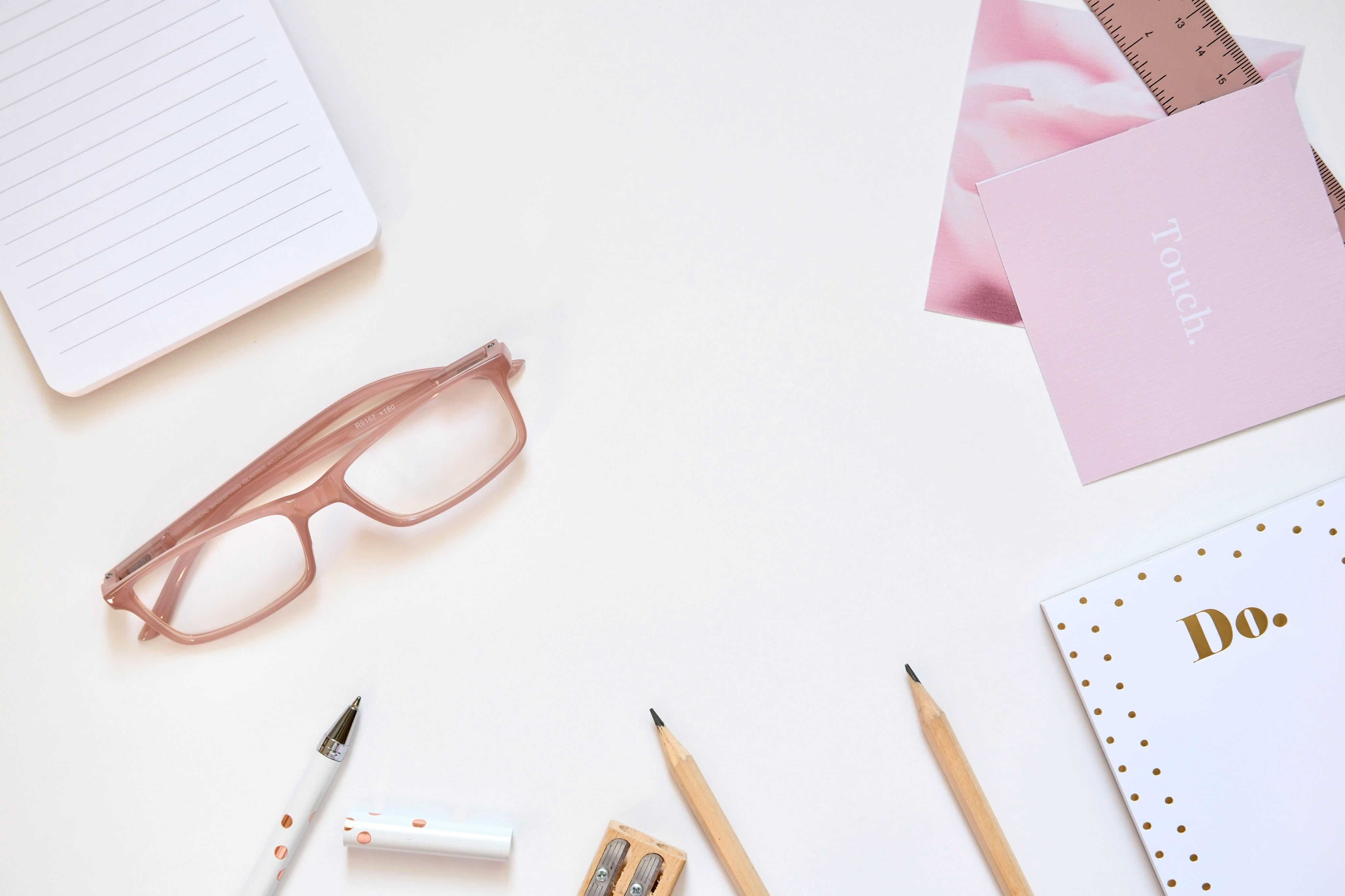 Stylish flat lay of stationery items and glasses on a white desk.