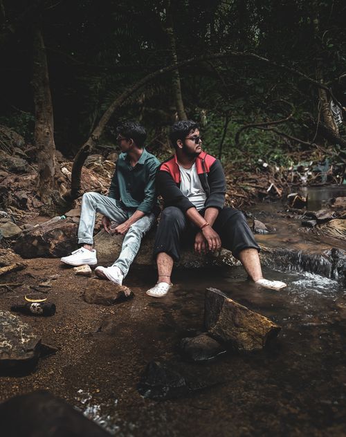 Free Two young men sitting by a stream, surrounded by nature in Bengaluru. Stock Photo