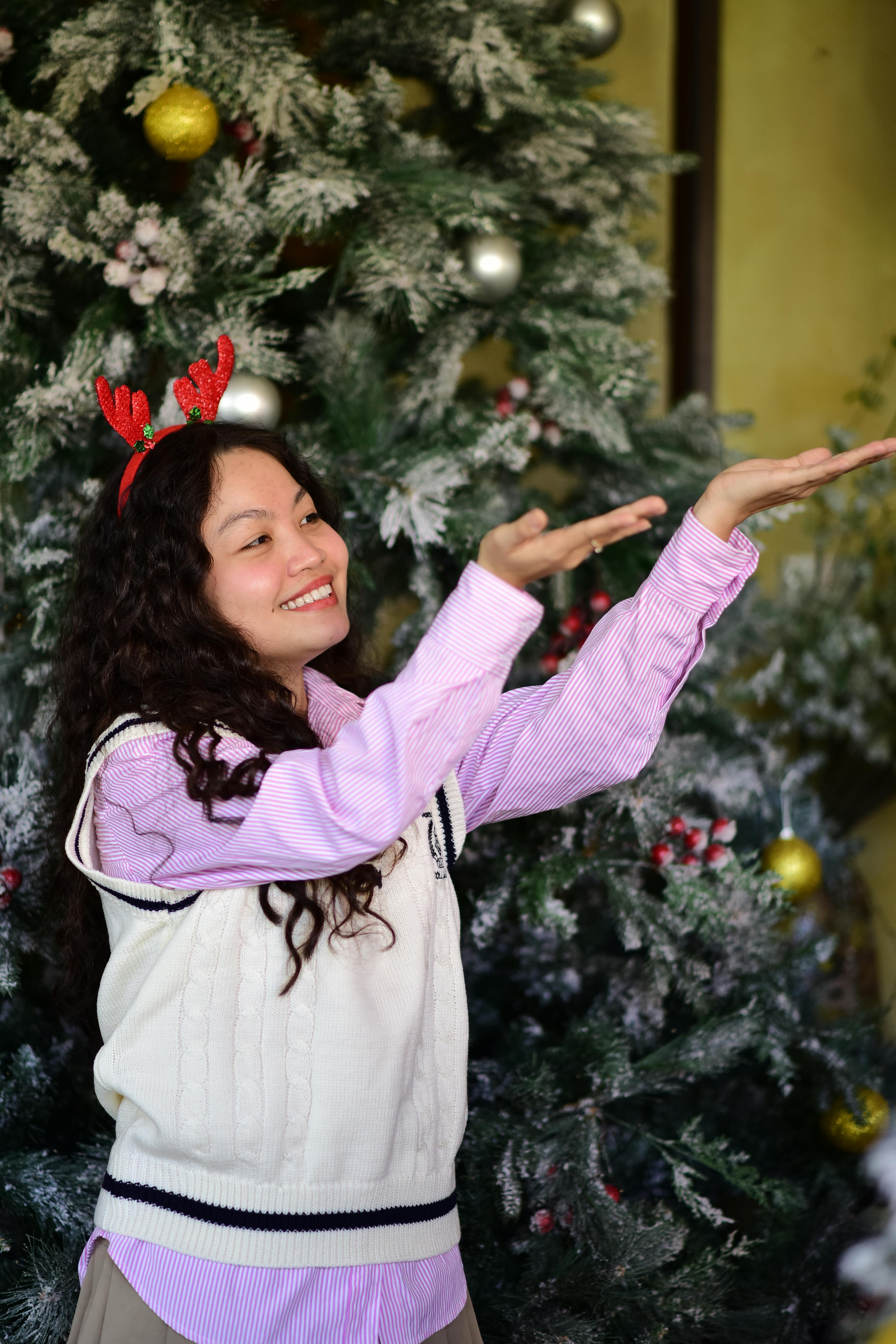 De franc Dona somrient amb banyes de ren posant al costat d'un arbre de Nadal decorat a l'interior. Foto d'estoc
