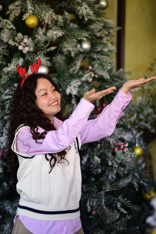 Free Smiling woman with reindeer antlers posing by a decorated Christmas tree indoors. Stock Photo