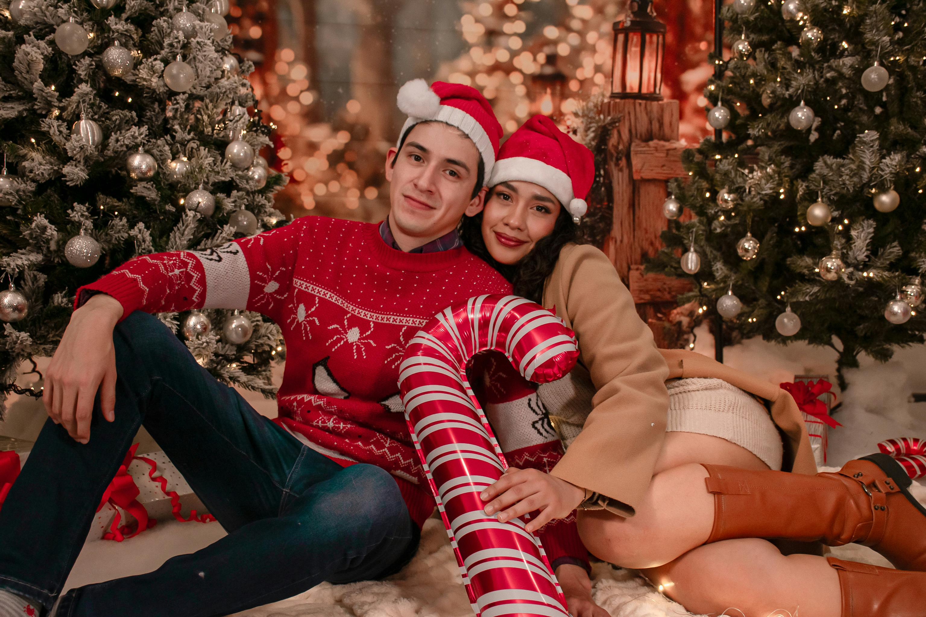 A joyful couple wearing Santa hats enjoys Christmas surrounded by festive decorations indoors.