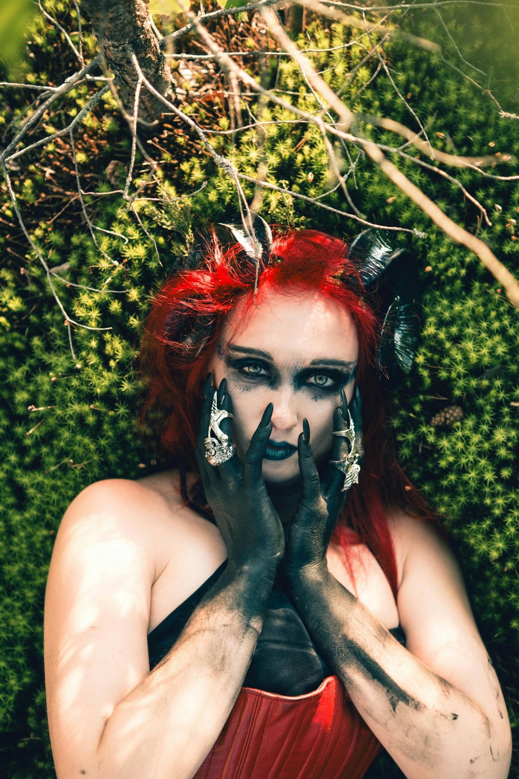 grátis Retrato encantador de uma mulher em traje de fantasia, com cabelos vermelhos e maquiagem preta, em meio a uma floresta. Foto profissional