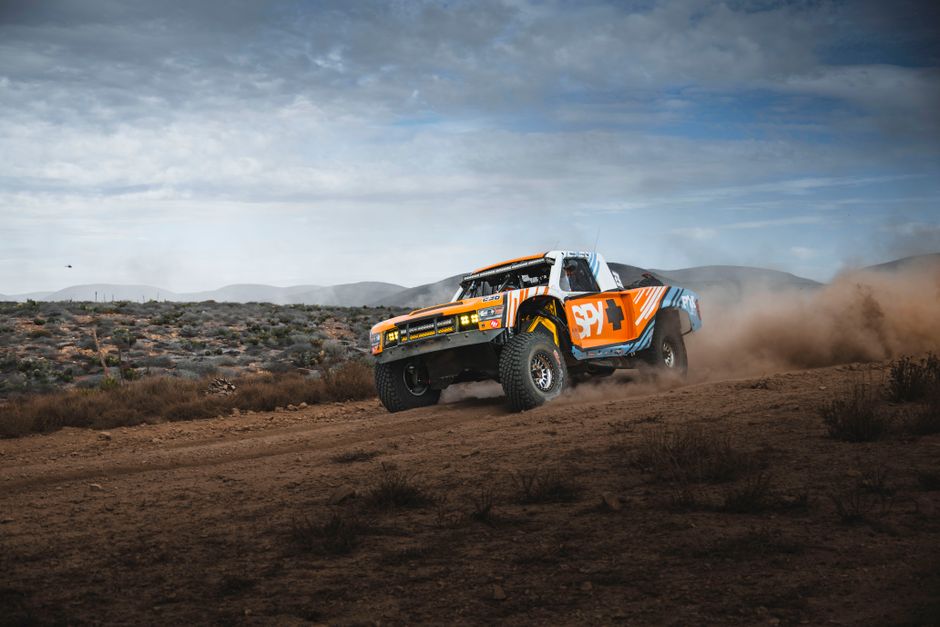 High-speed off-road rally truck kicking up dust in Baja California's rugged desert.