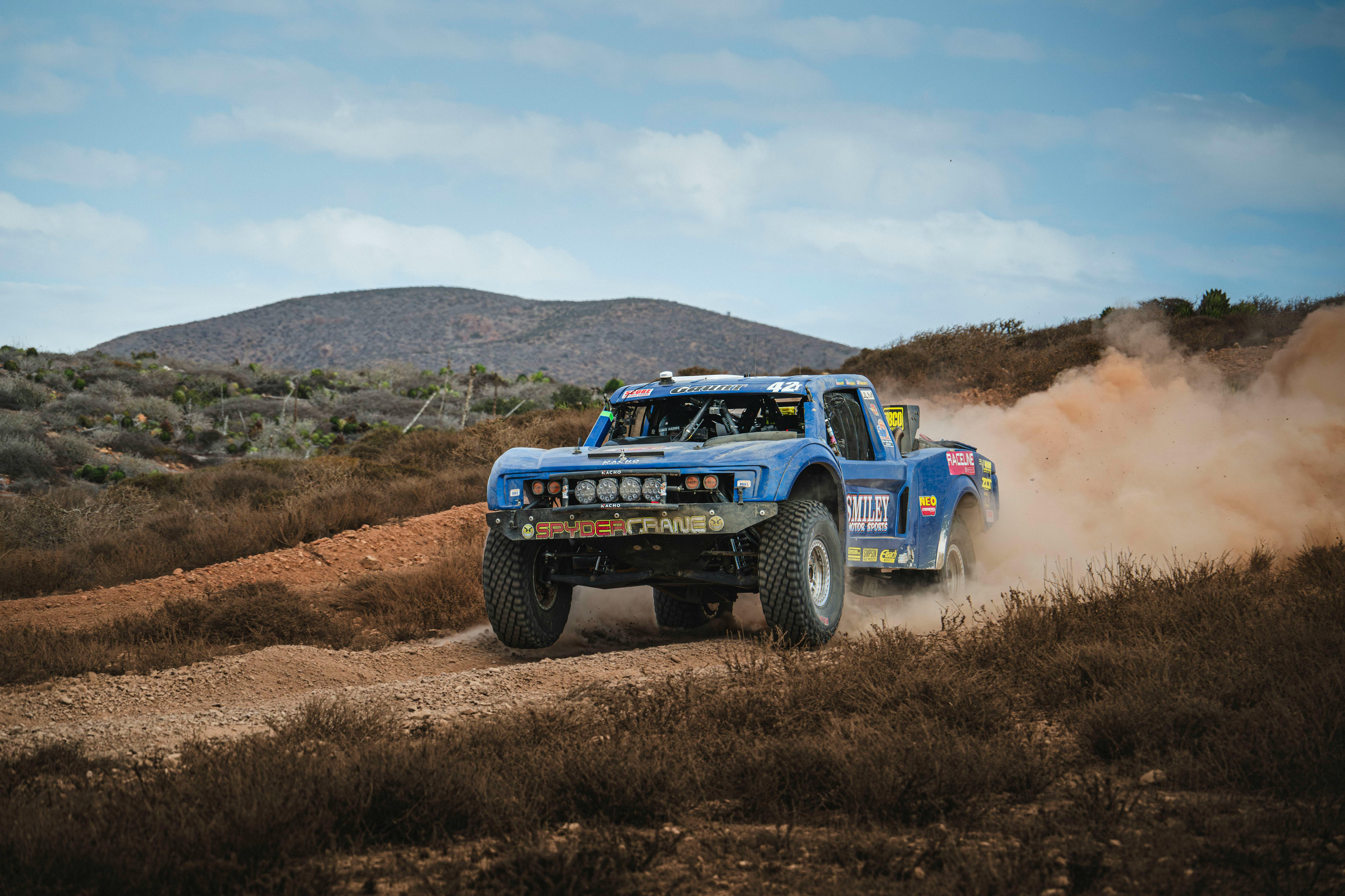 Off-road rally truck kicking up dust at high speed in the Baja California desert.