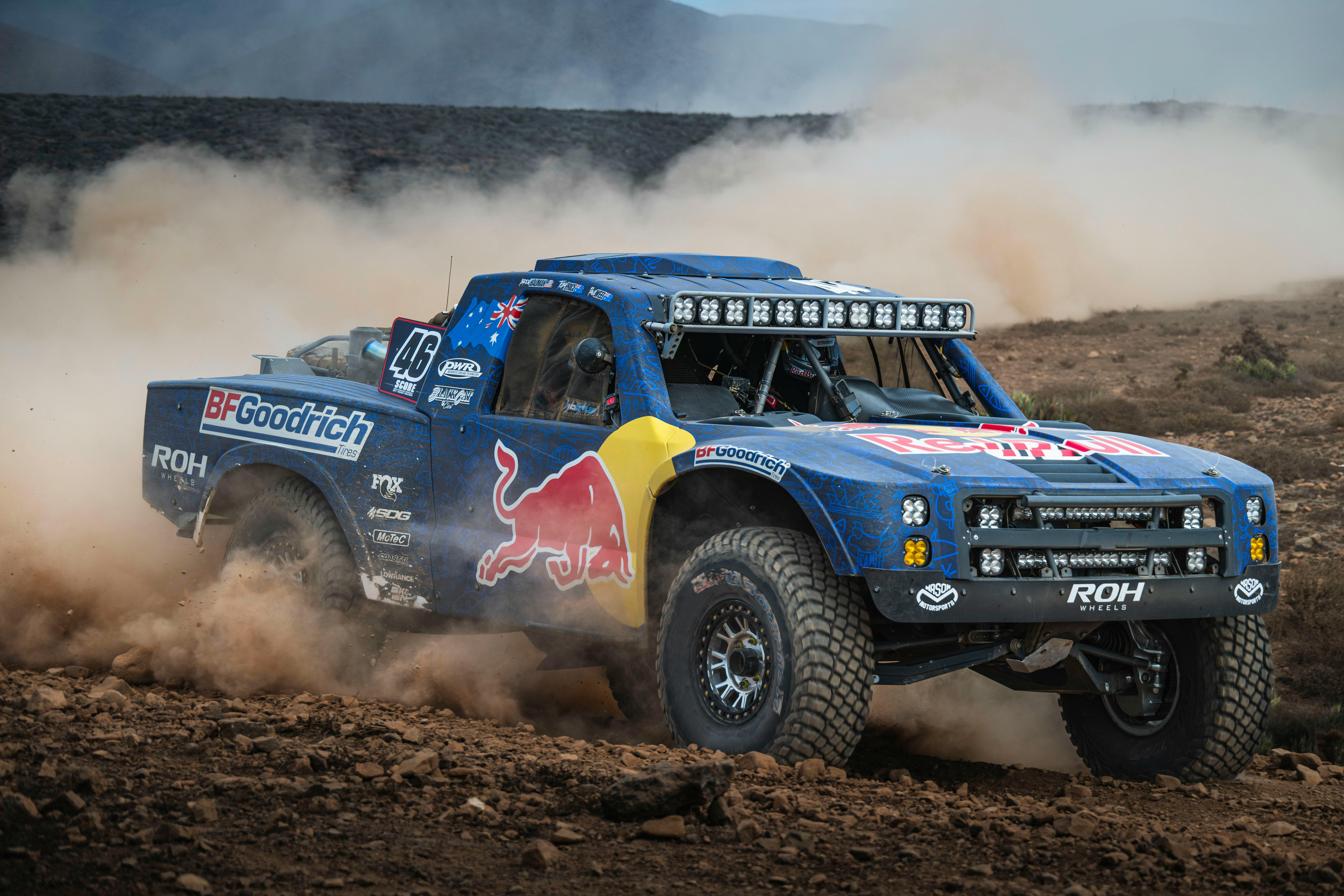 High-speed off-road truck race in Baja California desert, kicking up dust trails.
