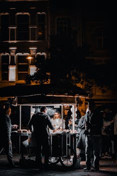 Bustling nighttime street market with people around an illuminated food stall.