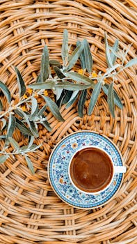 Artistic coffee cup with floral design on wicker surface, accented by foliage.
