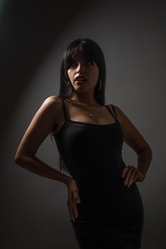 Stylish woman posing in dramatic lighting, wearing a sleek black dress.